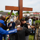 Several people stand around a giant cross marking a memorial for the people who died at the Buffalo shooting in May. They have their heads bent as they pray.